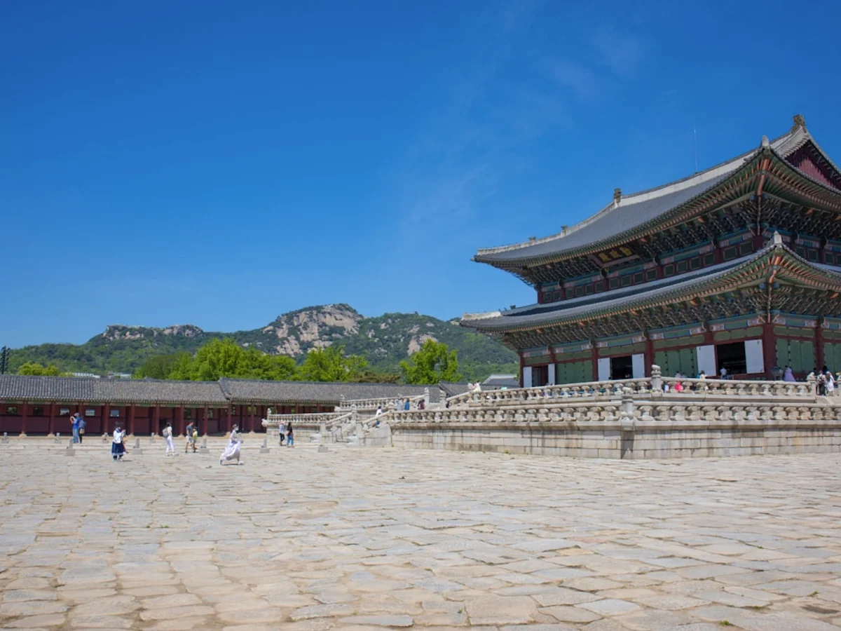 Korean street scene illustrating Essential visitor guide to Seoul's main royal palace, covering ticket prices, opening hours, free guided tours, and the best photography spots wearing traditional dress.